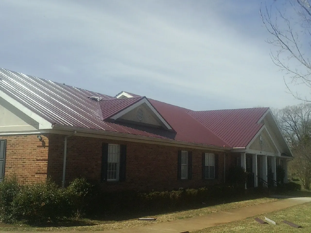 Red metal roof with gabled entries on a long brick building, from a Hail Damage Roof Repair job in Smallwood