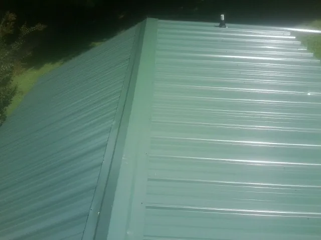 New green metal panels meeting at the ridge of a roof — Flat Roof Repair work by our crew in Smallwood