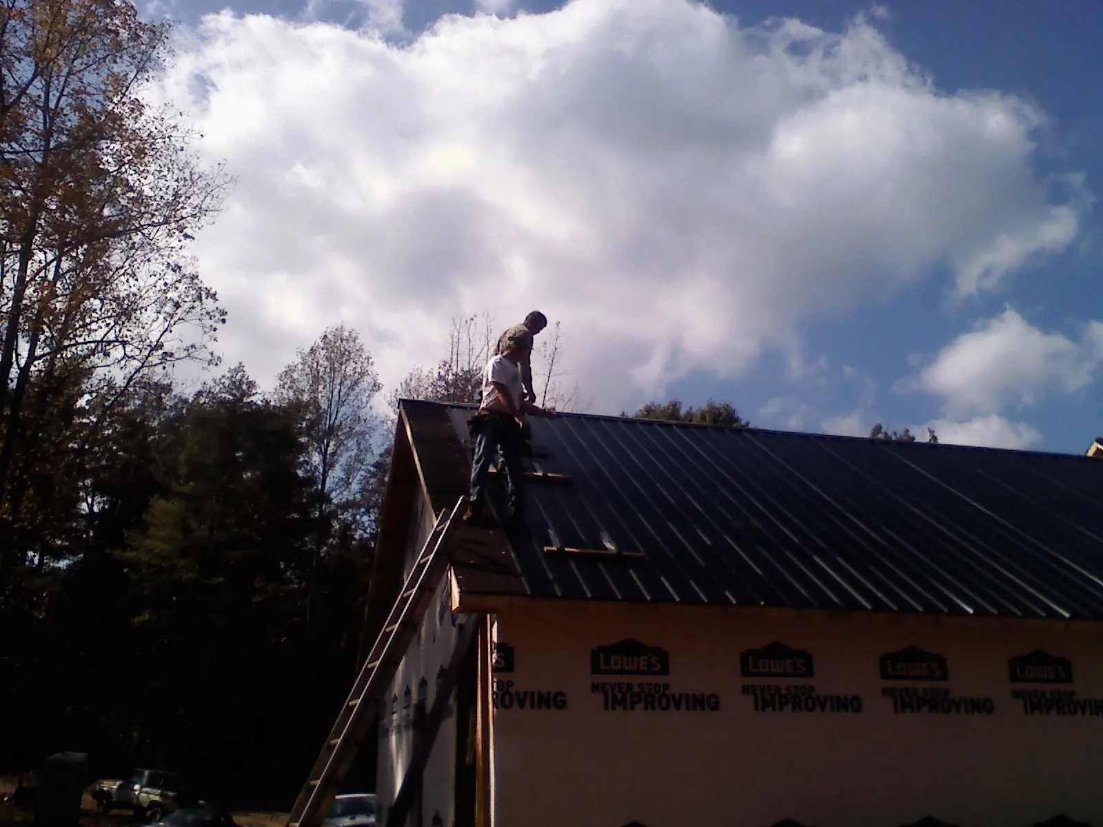 Roofer fastening dark metal panels high against a cloudy sky, from a Roof Inspection job in Smallwood