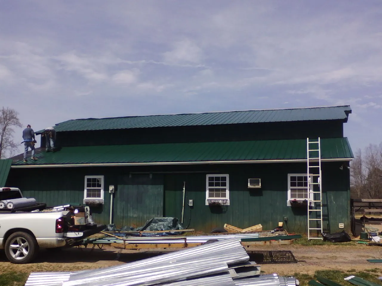 Crew installing green metal roofing on a large green barn in Smallwood
