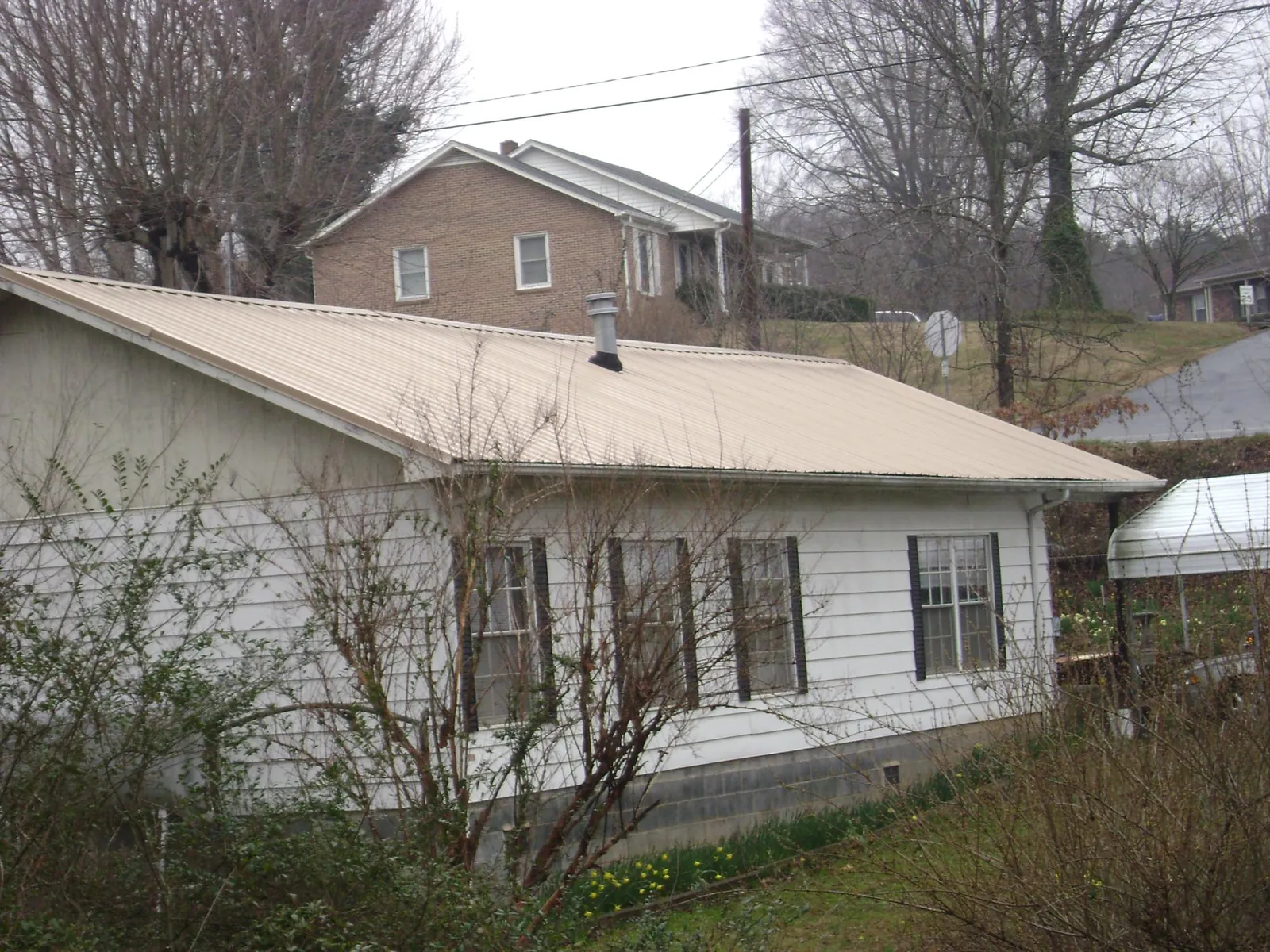 Tan metal roof on a white sided house set into a hillside — Commercial Roofing by Roofing Brothers in Smallwood